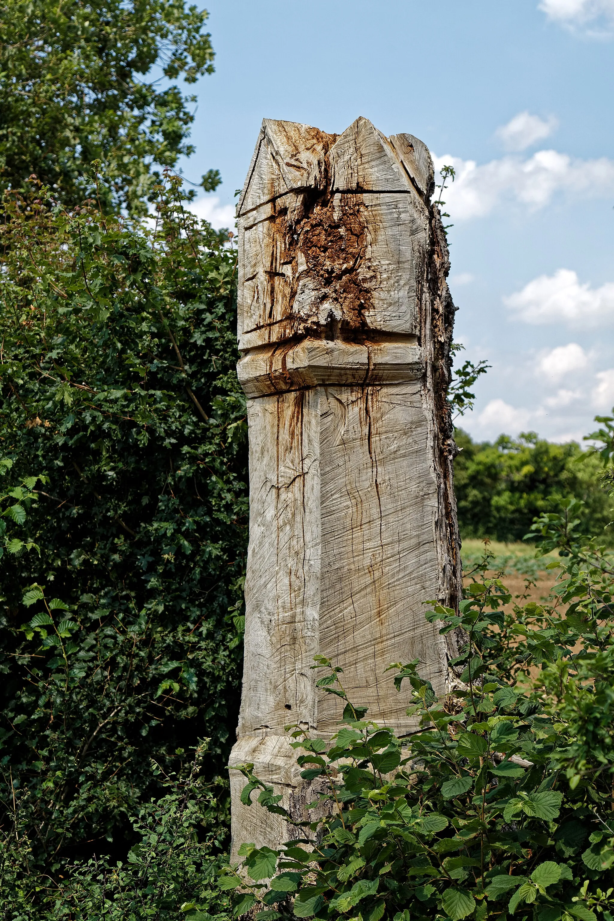 Photo showing: The dead trunk of a roadside oak tree carved by chainsaw into what appears to be imitating a gothic architectural structure, with gables and what looks like a sundial, to the north of Taverners Green in the parish of Hatfield Broad Oak, in Essex, England. Mobile device view: Wikimedia (June 2020) makes it difficult to immediately view photo groups related to this image. To see its most relevant allied photos, click on Hatfield Broad Oak, and this uploader's Photos. You can add a click-through 'categories' button to the very bottom of photo-pages you view by going to settings... three-bar icon top left. Desktop view: Wikimedia (June 2020) makes it difficult to immediately view the helpful category links where you can find images related to this one in a variety of ways; for these go to the very bottom of the page. This image is one of a series of date and/or subject allied consecutive photographs kept in progression or location by file name number and/or time marking. Camera: Canon EOS 6D Mark II with Canon EF 24-105mm F4L IS USM lens. Software: File lens-corrected, optimized, perhaps cropped, with DxO OpticsPro Elite, and likely further optimized with Adobe Photoshop CS2.