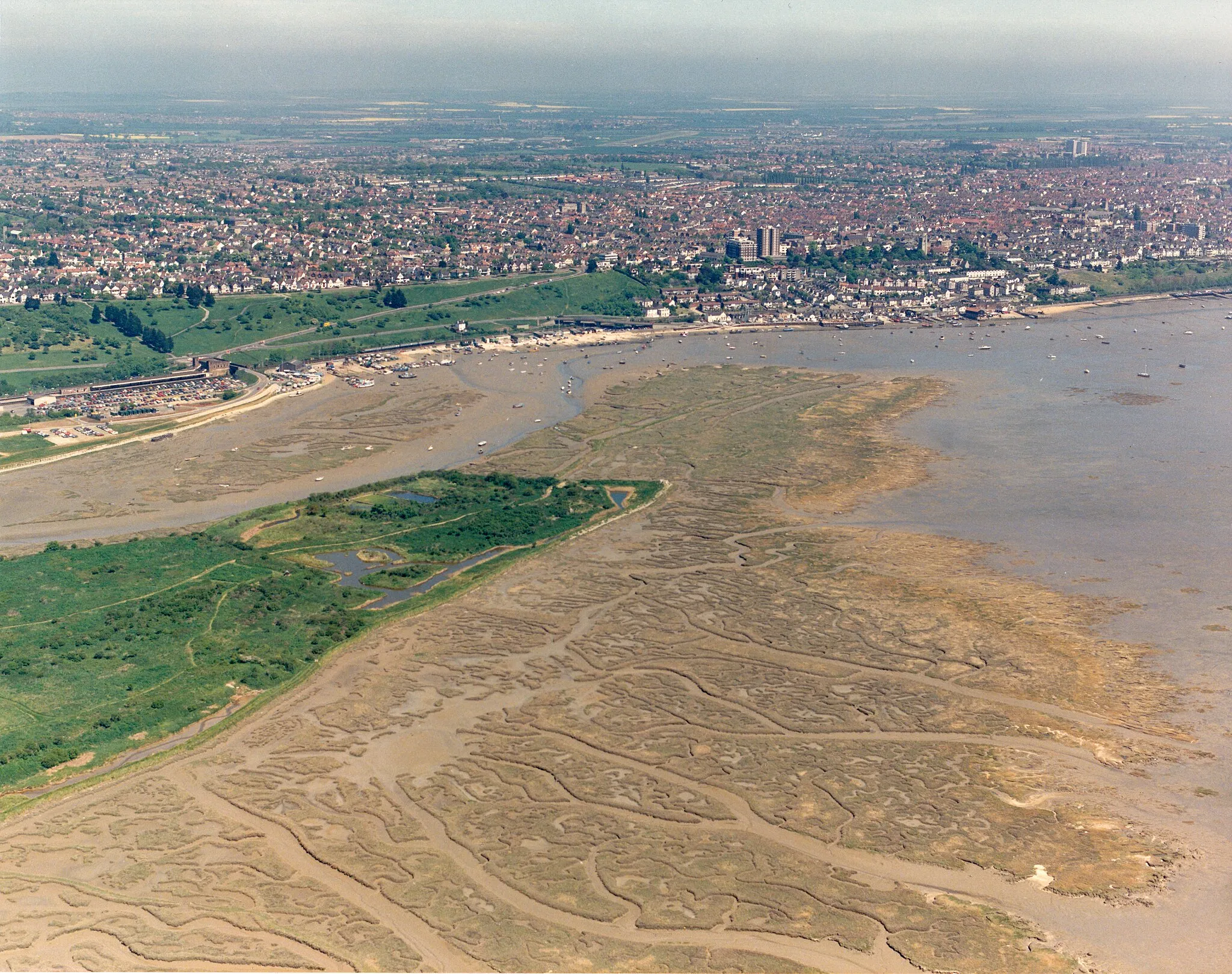 Photo showing: Aerial view of Two-Tree Island, eastern tip The eastern tip of Two-Tree Island lies within square TQ8385. It has a series of pools and dykes which attract birds, especially in the autumn. The extensive salt marsh to the right is rather bleached in August, but will form a roosting area for waders in winter at high tide. The buildings at the centre-right are those around Leigh station. Behind then are the green Belton Hills. Further along the coast above right of centre is Old Leigh.