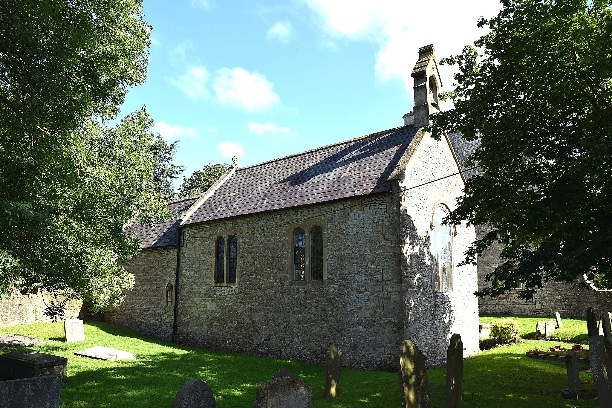 Photo showing: Burnett Church (St. Michael), 7 August 2016. The Historic England listing states that it is Early English 13th Century but another source state that it is Norman (1105) and I tend to favour the latter - the west window is Perpendicular but within a round headed arch which looks typically Norman. The nave has round headed twin lights although seemingly very heavily renovated in later Victorian times.