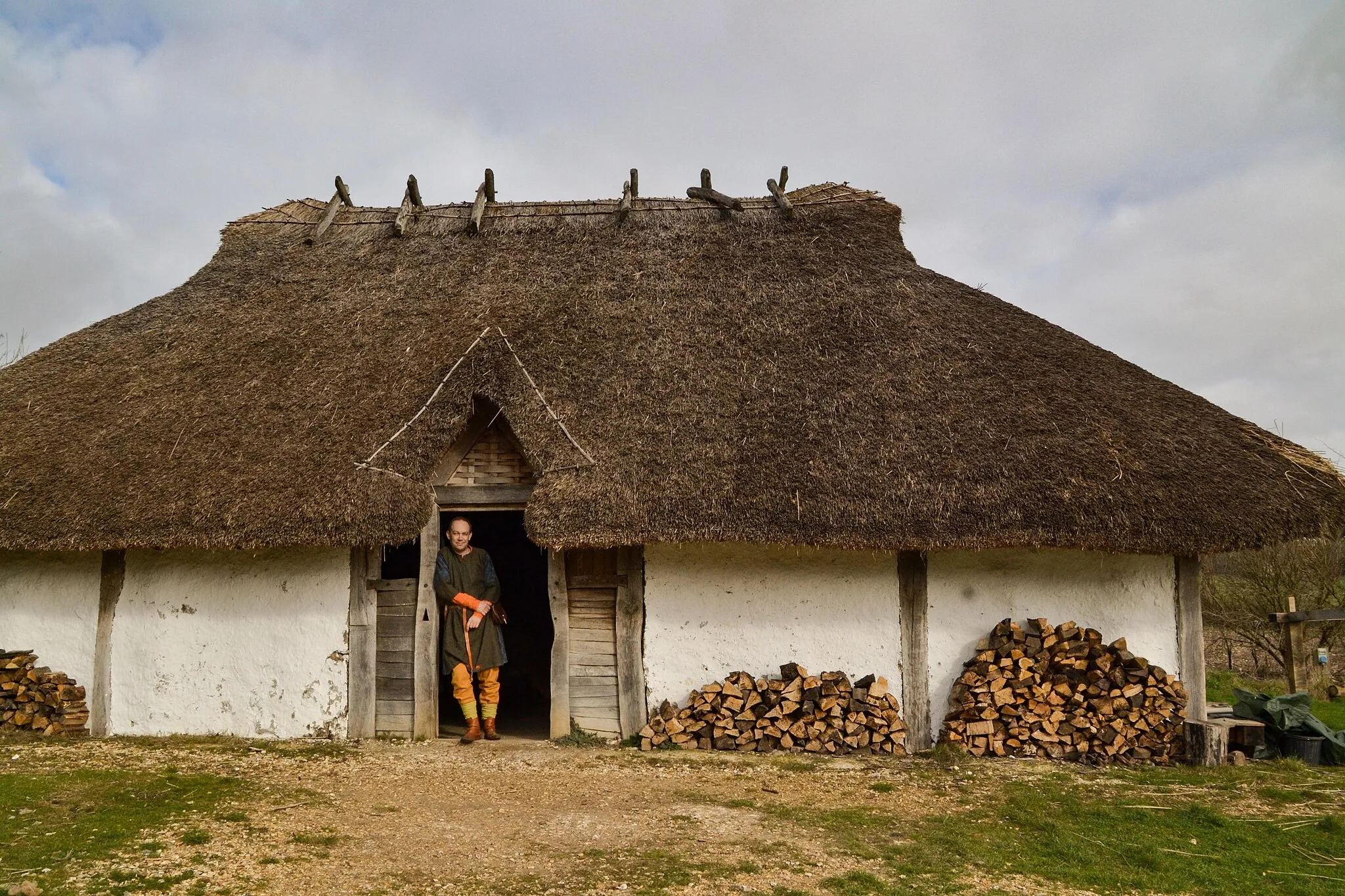 Photo showing: A re-enactor stands at the entrance to the Chalton A2 Saxon House reconstruction at Butser Ancient Farm