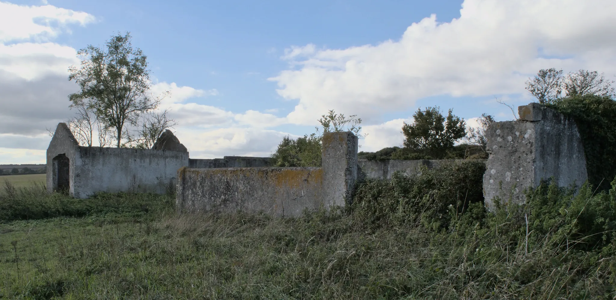 Photo showing: A front view of an abandoned concrete farm building on Abbotstone down with significant vegetation growing through within building elements.