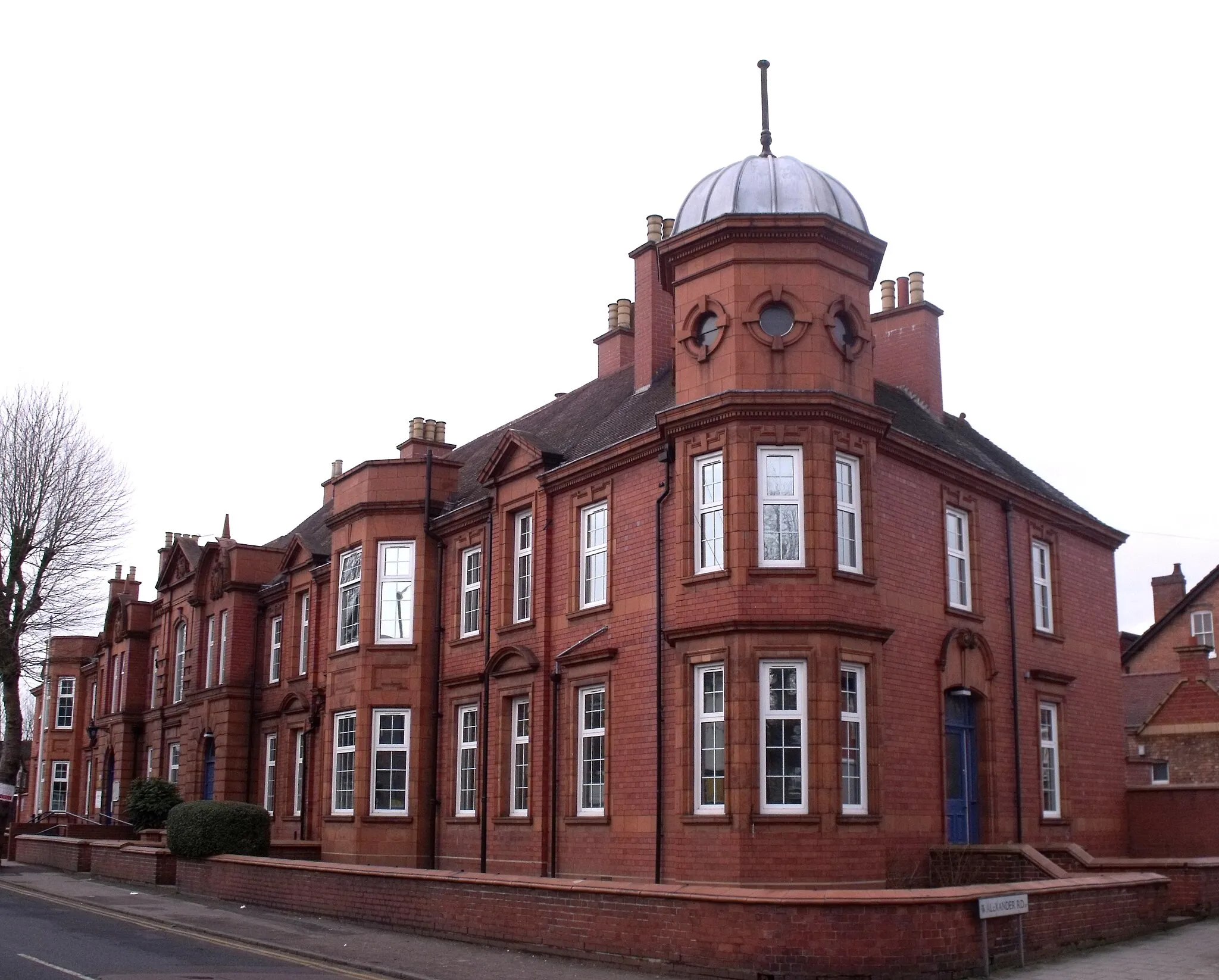 Photo showing: The red brick Acocks Green Police Station on Yardley Road in Acocks Green, Birmingham, England.
It is locally listed as Grade B.
It was built in 1909 for Yardley Rural District Council. It includes a Courthouse. Made of red brick and terracotta with a tile roof. Two-storeys. Almost symmetrical elevation to Yardley Road. Central section with rusticated ground floor, above which is a central pedimented bay with flanking projecting bays with segmental pediments. To either side are two-storey canted bays. Sliding sash windows throughout. On corner with Alexander Road is an octagonal turret with lead dome and keyed ocular windows. Low boundary wall with mould terracotta coping.

This shows the octagonal turret  on the corner of Alexander Road.