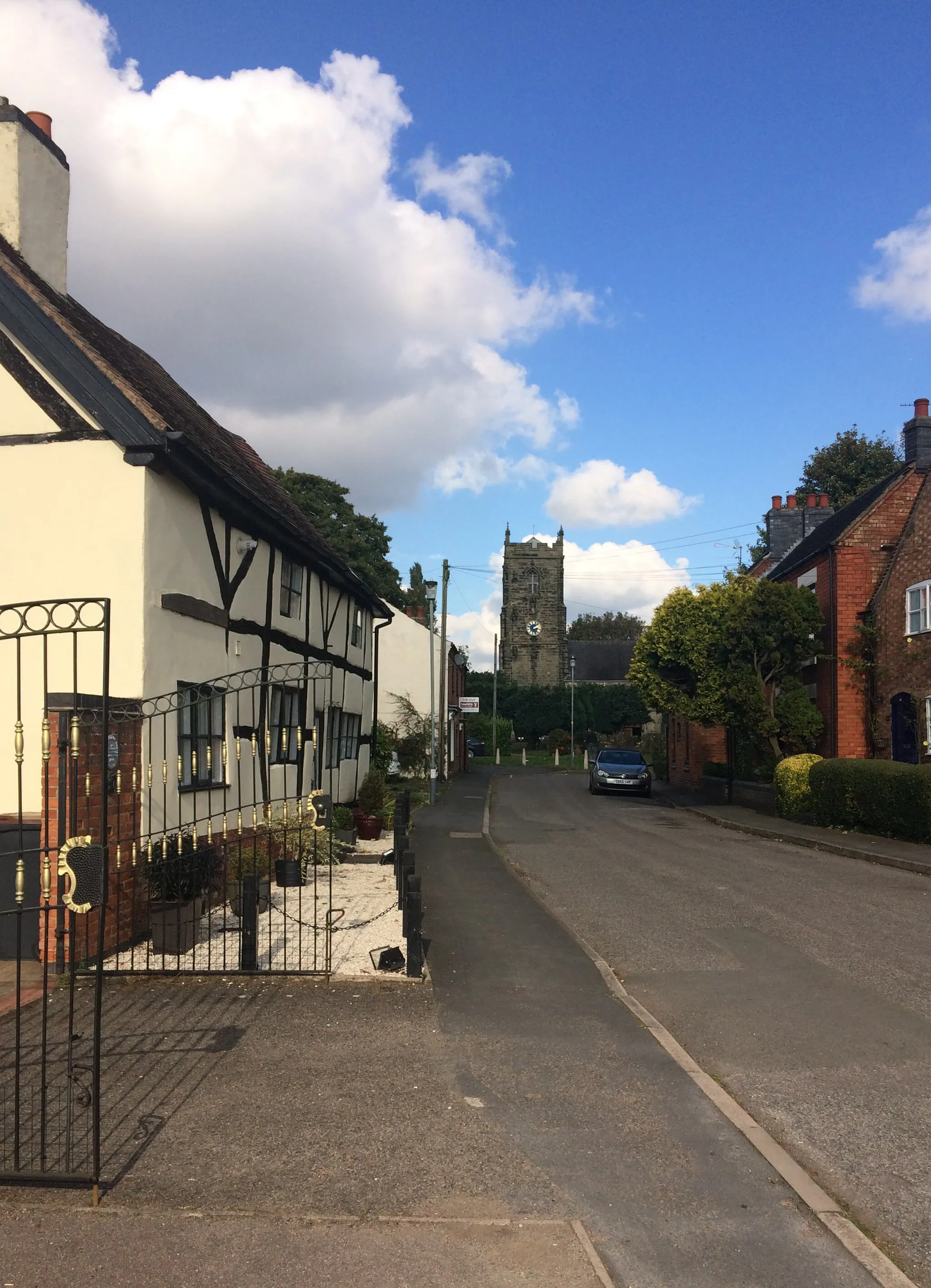 Photo showing: View north along Church Street, Bulkington, Warwickshire. The timber-framed cottages on the left are 3 and 4 Church Street. At the end of the street is the west tower of St James' parish church.