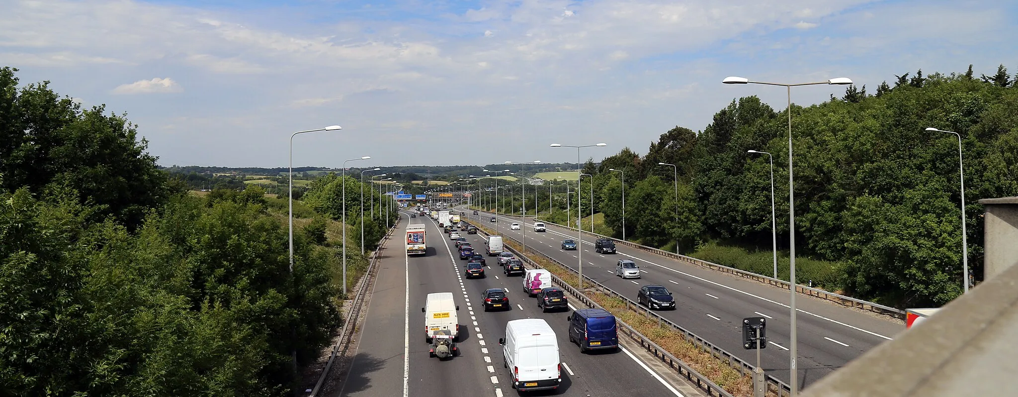 Photo showing: The M11 motorway looking north from a bridge on Coopersale Lane towards the M11 Junction 6 and M25 Junction 27 interchange, in the civil parish of Theydon Garnon, Essex, England
