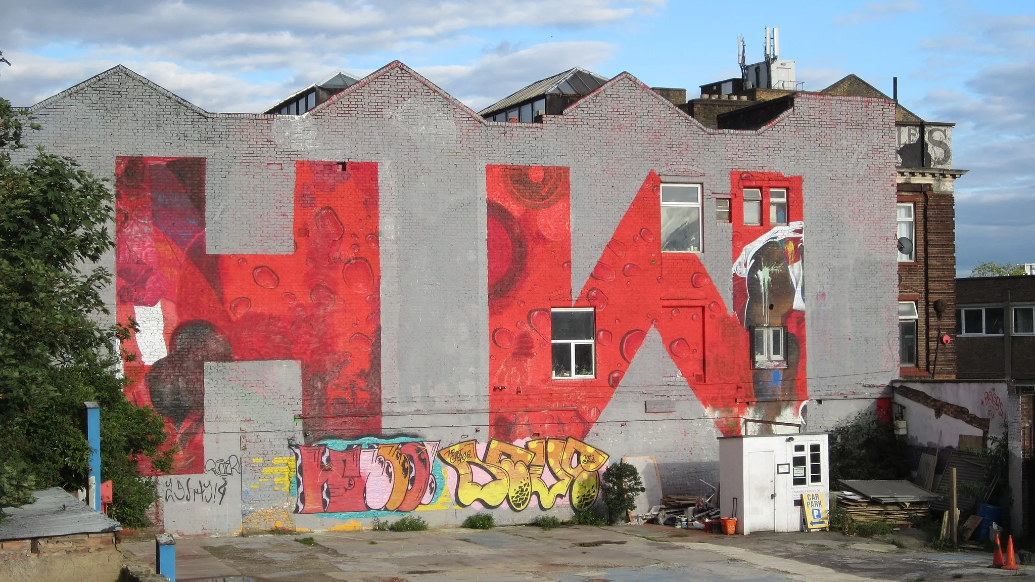 Photo showing: Photo of the Hackney Wick Coca Cola mural, taken in September 2013. The Coca Cola advertisement was painted in February 2012, in advance of the London Olympic Games hosted nearby. The advertisement was defiled by local artists and eventually over painted with the HW initials.