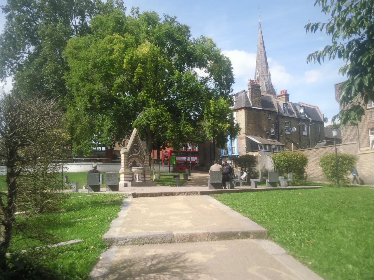 Photo showing: Part of Streatham Green, London SW16, looking north to the Dyce Drinking Fountain (left) and spire of the Roman Catholic church of the English Martyrs. The Dyce Fountain was moved here in 1933 from Streatham High Road.