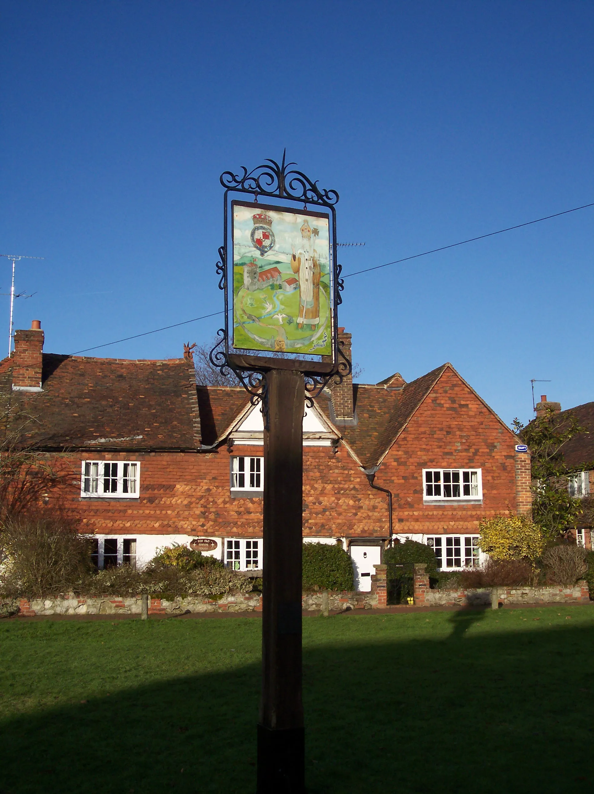 Photo showing: Brasted Village Sign On the village Green at the junction of the A25 Brasted High Street (in front) and Rectory Lane (on the left). In the background is the Old Manor House.
On the post is a plaque which reads 'A mediaeval archbishop of Canterbury stands
in the "Garden" of Brasted in the attitude of blessing. Because in AD 773 the manor was given by Offa, King of Mercia to the Friary of Christchurch Canterbury under which it remained until the conquest and soon after
William I's death it passed to the Clare Family, Who held it of the Archbishop of Canterbury 'in grand sergeantry' The Connection with Canterbury still continues, because Brasted, Sundridge and Chevening are known as "the Archbishop's Garden" and their livings remain in his gift.
Brasted Church is depicted here as well as the River Darent and its bridges; the North Downs form a background with the Pilgrim's Way below them. Leading to the distant towers of Canterbury. The shield of Arms surrounded by the Ribbon
of the Garter is that of the 7th Earl Stanhope K.G. Lord of the Manor of Brasted in 1951.
This sign was designed and painted by G. Andrew McShane

and restored by Antique Restorations, Brasted 1991'