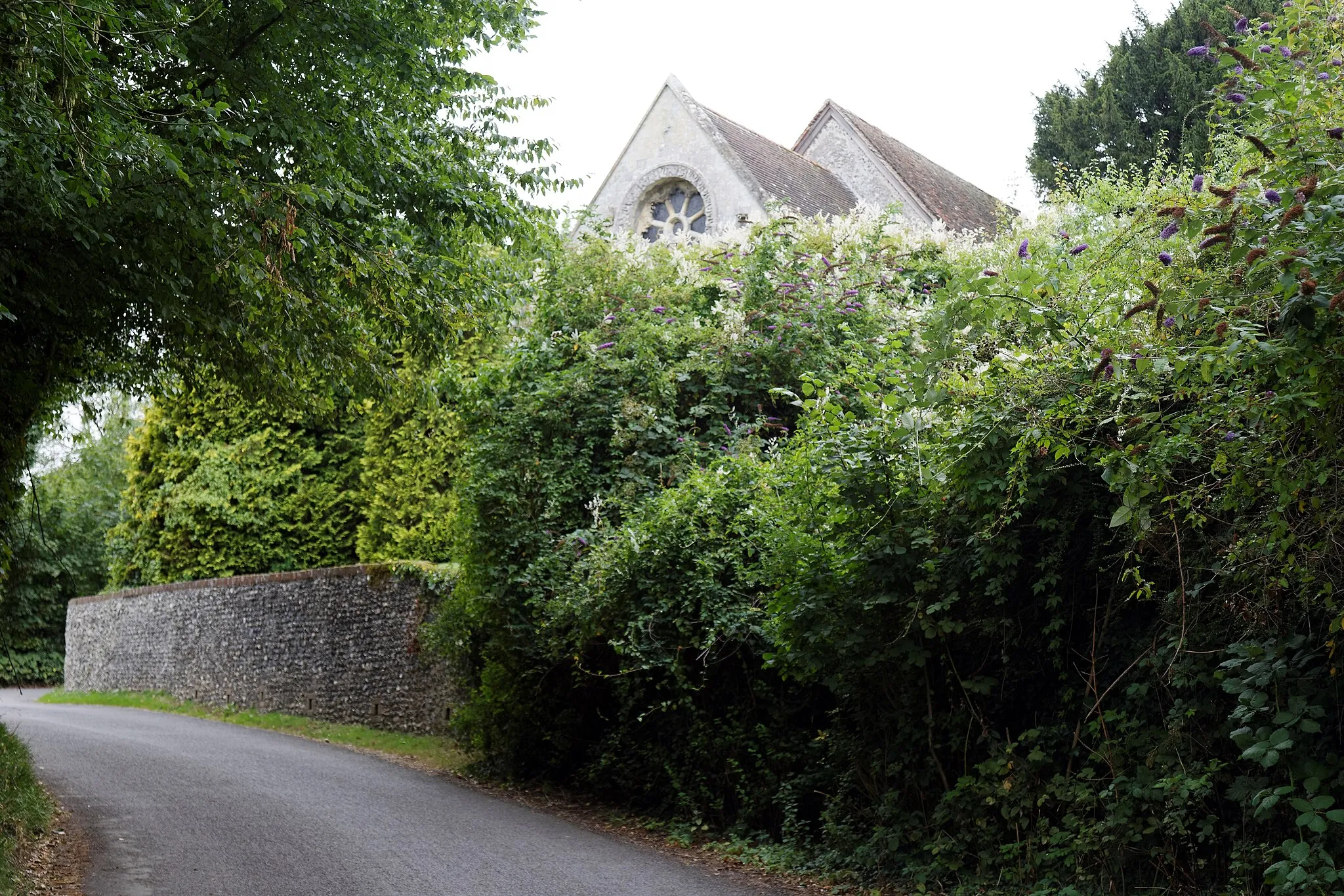 Photo showing: View from north east of St Nicholas' Church with road, trees, shrub hedges and flint wall at Barfrestone in Kent, England. Software: RAW file lens-corrected, optimized and converted to JPEG with DxO OpticsPro 10 Elite, and likely further optimized and/or cropped and/or spun with Adobe Photoshop CS2.