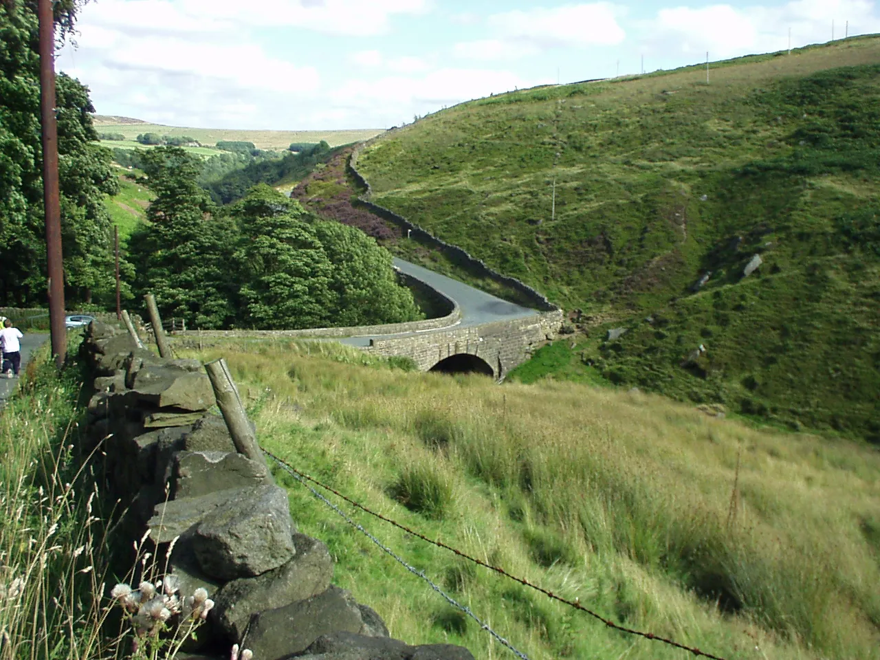 Photo showing: Blake Dean (Black Dean) Looking east. The area on the right (west) side of the bridge is shown on modern OS maps as Blake Dean. Below the bridge, after the confluence with Alcomden Water the clough is recorded as Black Dean. Historical OS maps call the whole area Black Dean. The element 'black' may mean a pass - from the Celtic 'bealach' meaning a pass or an entrance from one district to another or may be descriptive of the peaty colour of the water here. The road that crosses the clough here runs from Heptonstall to Widdop and on into Lancashire