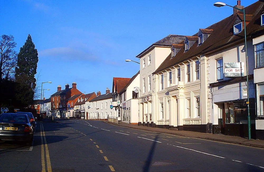 Photo showing: Market Hill in the town centre of Southam, Warwickshire, England. This is the main street through the town and used to be a main road before Southam was bypassed. At the left is the site of the old town market.