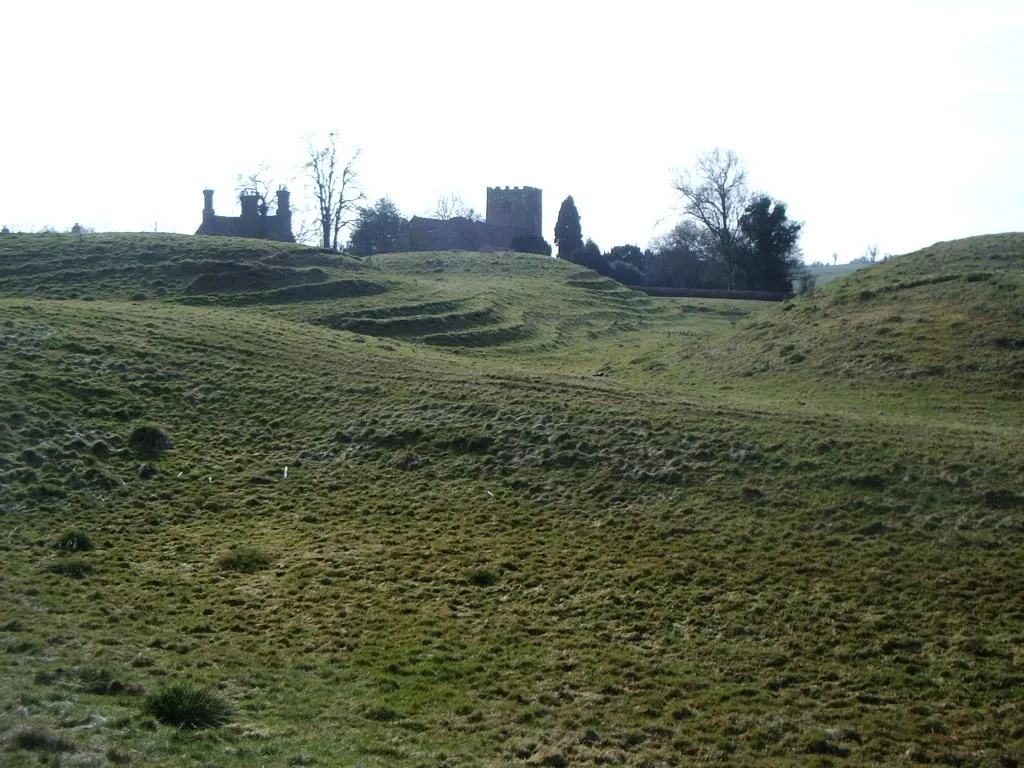 Photo showing: Castle and motte, Lilbourne View from field boundary of castle motte remains and Lilbourne church beyond.