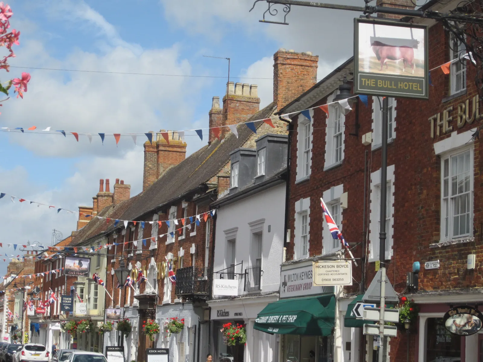 Photo showing: High Street, Stony Stratford, Buckinghamshire, England. Stony Stratford is a constituent town of Milton Keynes but it was once an important town in its own right, a coaching stop a day's journey from London by stage-coach on the London-Birmingham Turnpike ((Watling Street, later to become the A5). The legacy of this role is two coaching inns on the High Street, the Bull (seen here in the foreground), and a little further along the Cock. They were known for the tales that travellers would tell and, it is said, gave rise to the expression 'Cock and Bull story'.