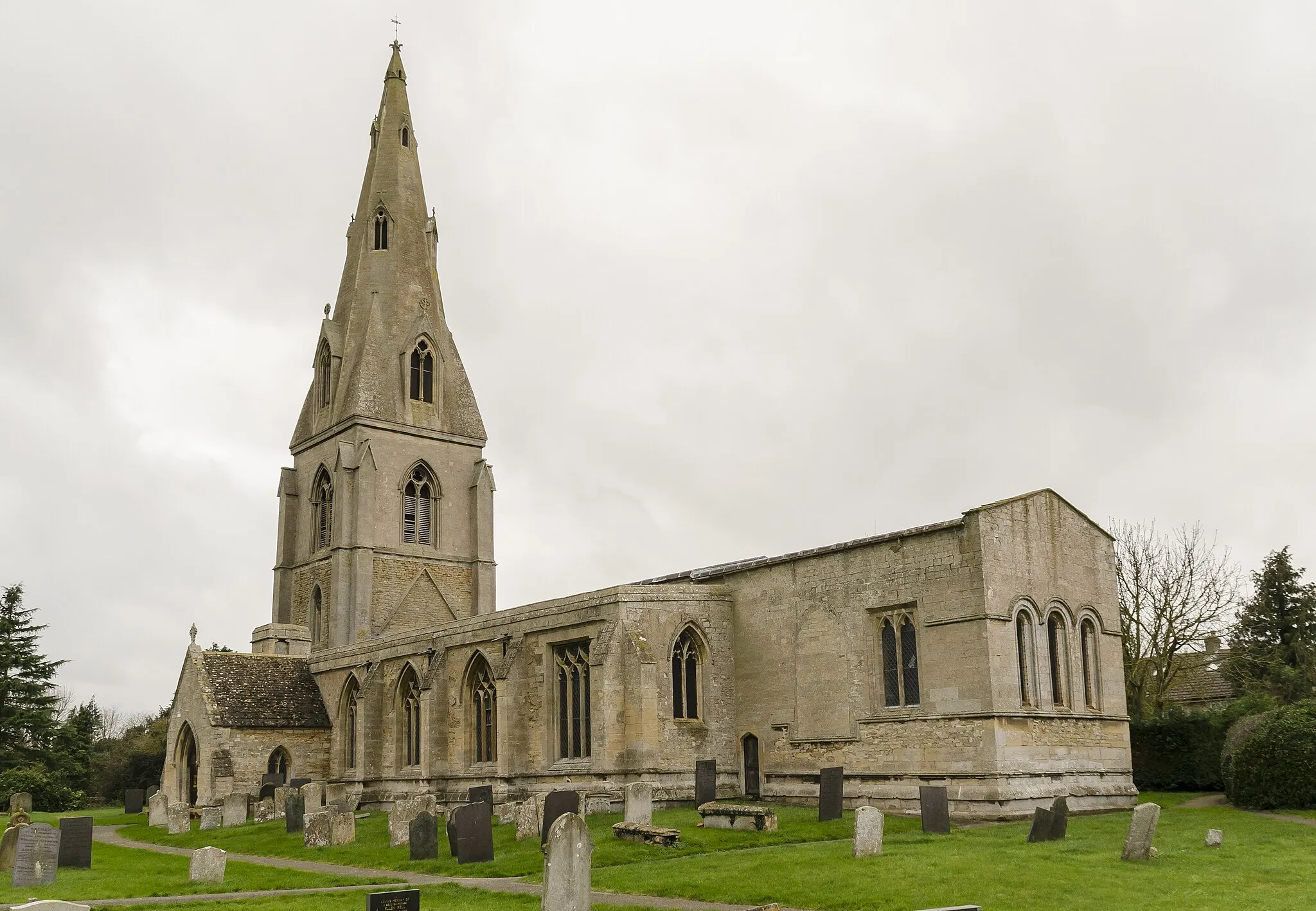 Photo showing: There was already a church on this site named St Peter in the Domesday Survey. It could have been a small Saxon church or a Danish church that was built by Cnut (when he was King of England) near to the site of the 869 battle. There is a strong likelihood that it was used as the foundation for the church that was built 90 years after the Survey was taken.
From a Charter issued by Henry II in 1154, we learn that Simon and Adelicia, the Earl and Countess de Gant (from the Manor House at Folkingham), took sole possession of the Threekingham churches. They, in turn, gave these churches and all their possessions to the recently opened Leper House at the Burton Lazars Monastery in Leicestershire. In about 1170 work started on a new church at Threekingham, and the tower and chancel that were erected then exist to this day. It is unlikely that the Burton Lazars Monastery could finance such an expensive undertaking, and it was most likely sponsored by the Gant family.
The church that resulted was larger than the previous one and built in a style now know as Late-Norman. The new St Peter's had a small chapel built onto the north side of the chancel and this remaind there until 1325 when it was demolished and the stones used to build the north aisle. The blocked up entrance is still visible. The nave was altered in 1280 and the south aisle and porch were added by the de Treckyngham family in 1310. The spire and buttresses were built in 1320. When the de Treckyngham family demolished the small chapel in 1325 they moved the effigies (dating from about 1280) of Sir Lambert & his wife from there to the eastern end of the north aisle where they created a small family chantry.

The final change to St Peter's external structure was the removal of the pitched roof and its wooden shingles in the 16th century. It was replaced by a much flatter roof that was covered in lead, which was last changed in the mid-20th century. The roof's internal structure is mostly original, but some of the wooden supports were replaced in the early 1960s. Internally the church remained as it was until 1859 when the Reverend Ellicott raised enough money for a restoration project that introduced the tiled floor and new pews. The old wooden pulpit was replaced in 1894 but the current marble one. The organ was built in 1906 and the effigies of Sir Lambert and his wife moved to their current resting place at the west end of the nave.