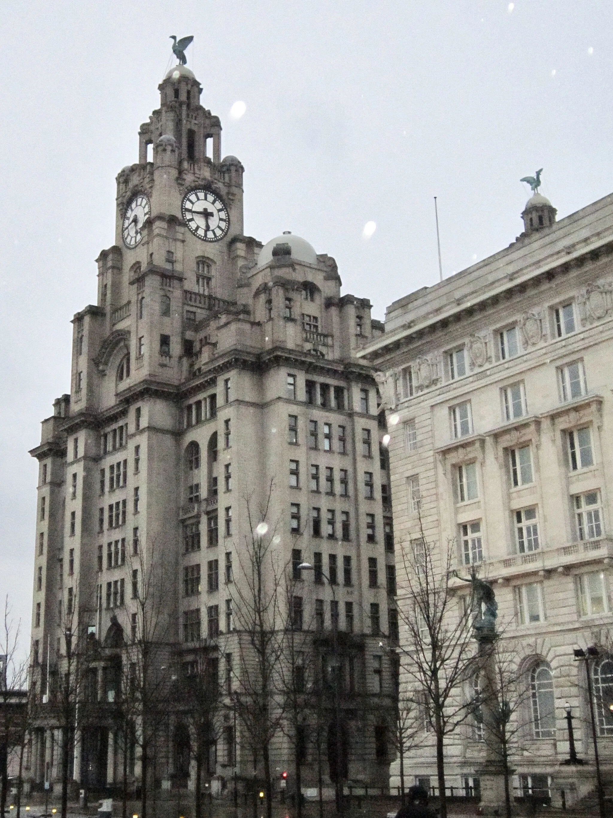 Photo showing: The Royal Liver Building is a Grade I listed building in Liverpool, England  and is a symbol of the Liverpool City Region, and so too, is the Liver Birds (sculptures) on top of the building.
The Liver Bird appears on the seals and logos for a plethora of businesses in the Liverpool Bay Area and on the Liverpool Football Club.
The Royal Liver Building has the largest clock faces in the UK.
The two Liver Birds(Mythical creatures) that stand proudly on top of the building, named Bertie and Bella, are said to protect the City. 
Bertie faces the city, keeping a watchful eye on the citizens of Liverpoool.
Legend has it that if those two the Liver Birds fly off, the City will cease to exist.
Royal Liver Building
Liverpool Watefront,
Liverpool, L3 1HU
England, United Kingdom
Architect- Walter Aubrey Thomas
Building Completion- 1911
http://www.royalliverbuilding.com/

https://www.visitliverpool.com/listing/royal-liver-building-360/44496101/