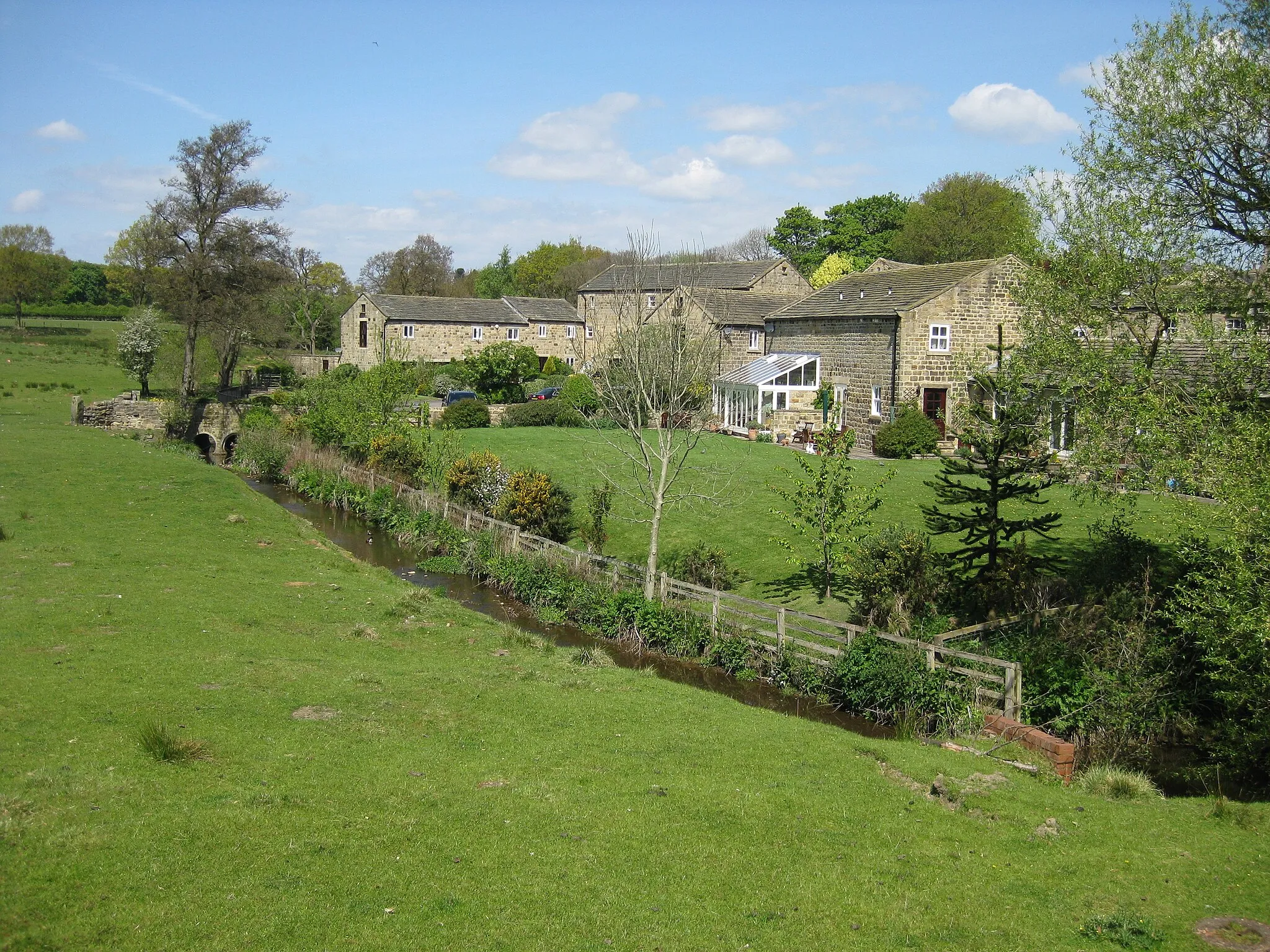 Photo showing: Adel Beck (stream) and buildings of the former Adel Mill Farm and millworkers cottages (now residences). A bridge over the stream .