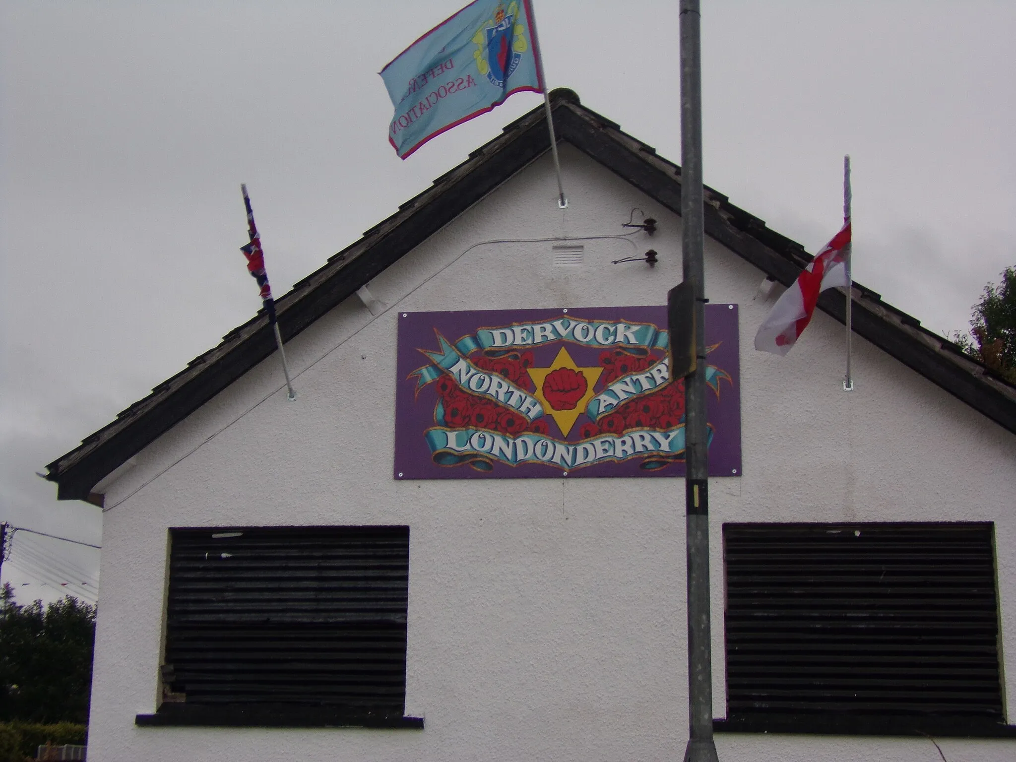 Photo showing: A wall sign in Dervock, County Antrim showing support for the loyalist paramilitary group the UDA.The North Antrim and Londonderry brigade of the UDA is listed on the sign.The flags flying above it are the UDA,Union and Ulster flags.