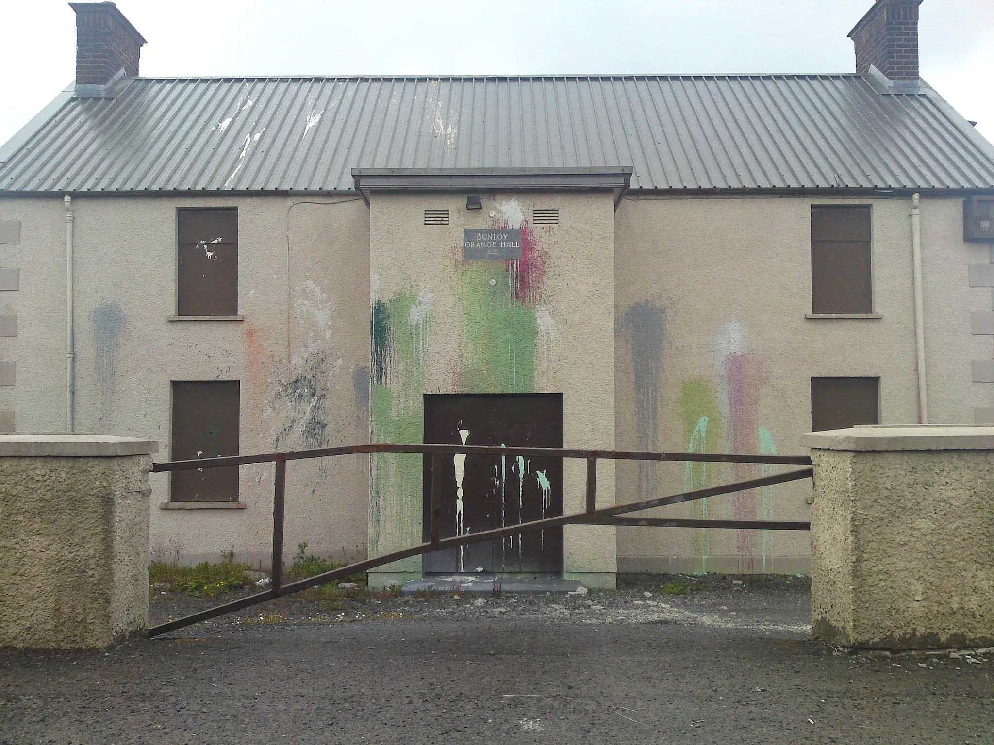 Photo showing: Dunloy Orange Hall.Siyuated on the Station Road just outside the village.It has been repeatedly attacked and covered in paint.The plaque above the door reads "Dunloy Orange Hall 1896"