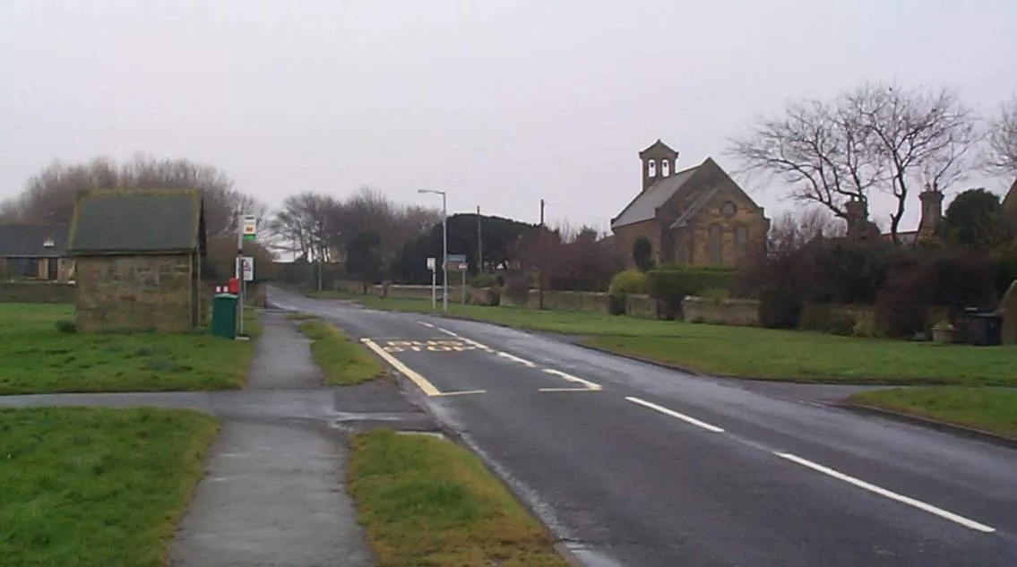Photo showing: View southwest along the main road in Cresswell, Northumberland, with St Bartholomew's parish church on the right