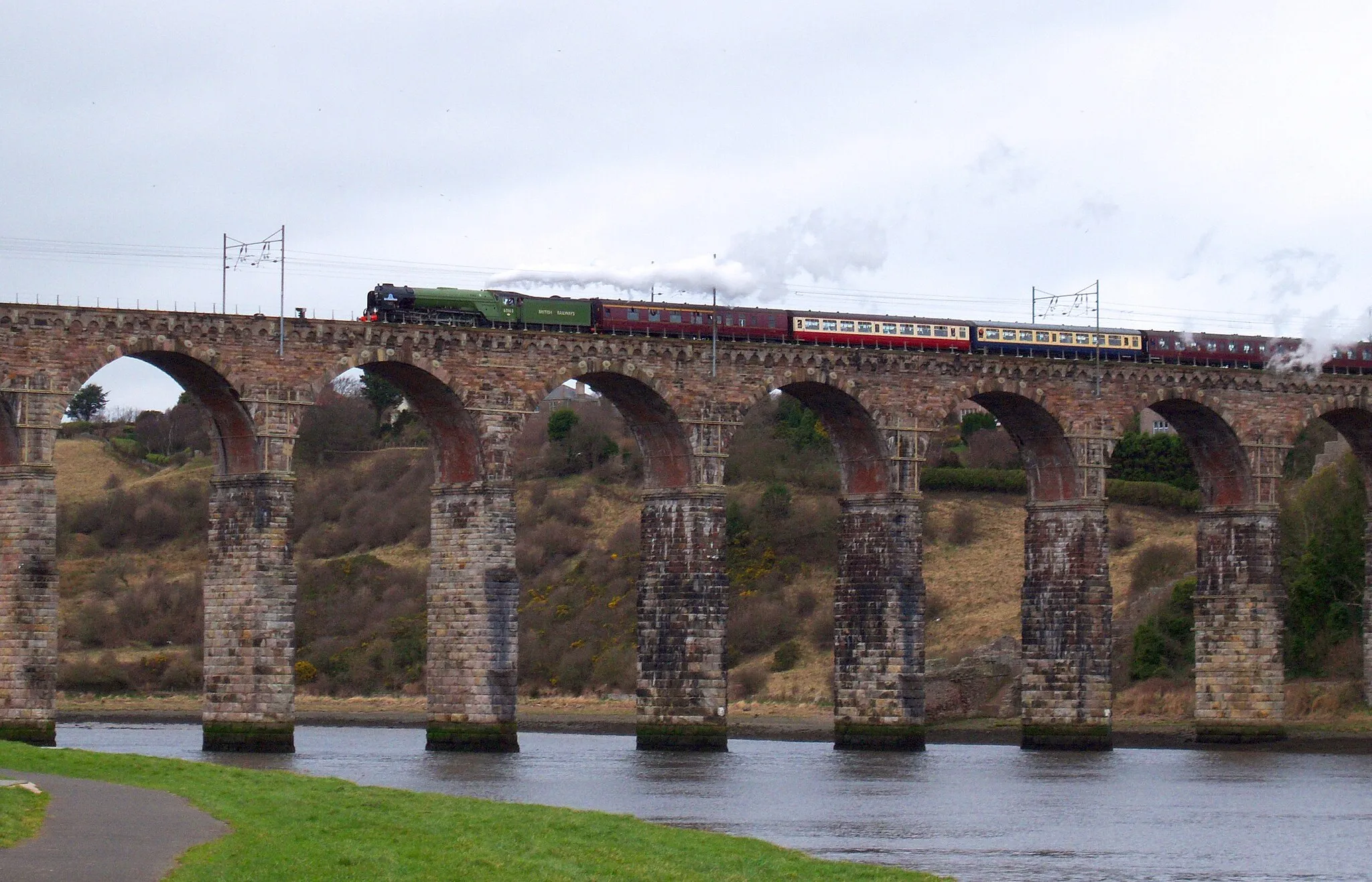 Photo showing: Brand new steam locomotive 60163 Tornado crosses the Royal Border Bridge railway viaduct in Berwick-upon-Tweed, travelling south at the head of The North Briton charter train from Edinburgh to York.
This was the first time Tornado had passed over the viaduct in the southbound direction, having crossed for the first time in northbound a week earlier, hauling The Auld Reekie Express from York to Edinburgh.
Tornado is brand new Peppercorn A1 class locomotive completed in 2008. The Peppercorn A1 was the last type of express passenger steam locomotive that was used on this route on the East Coast Main Line from Scotland to London. None of the original 49 survived the scrapyard in the change to diesel, and later, electric traction.
Tornado is coasting at this point, the steam above the locomotive is actually coming from the boiler safety valves and not the chimney, creating a false impression of a steam exhaust.

Taken at 15:12 GMT from the south bank of the River Tweed, east of the bridge, Tornado was approximately 15 minutes early for arrival in Berwick, and proceeded to Tweedmouth sidings on the other side of the bridge to take on water.