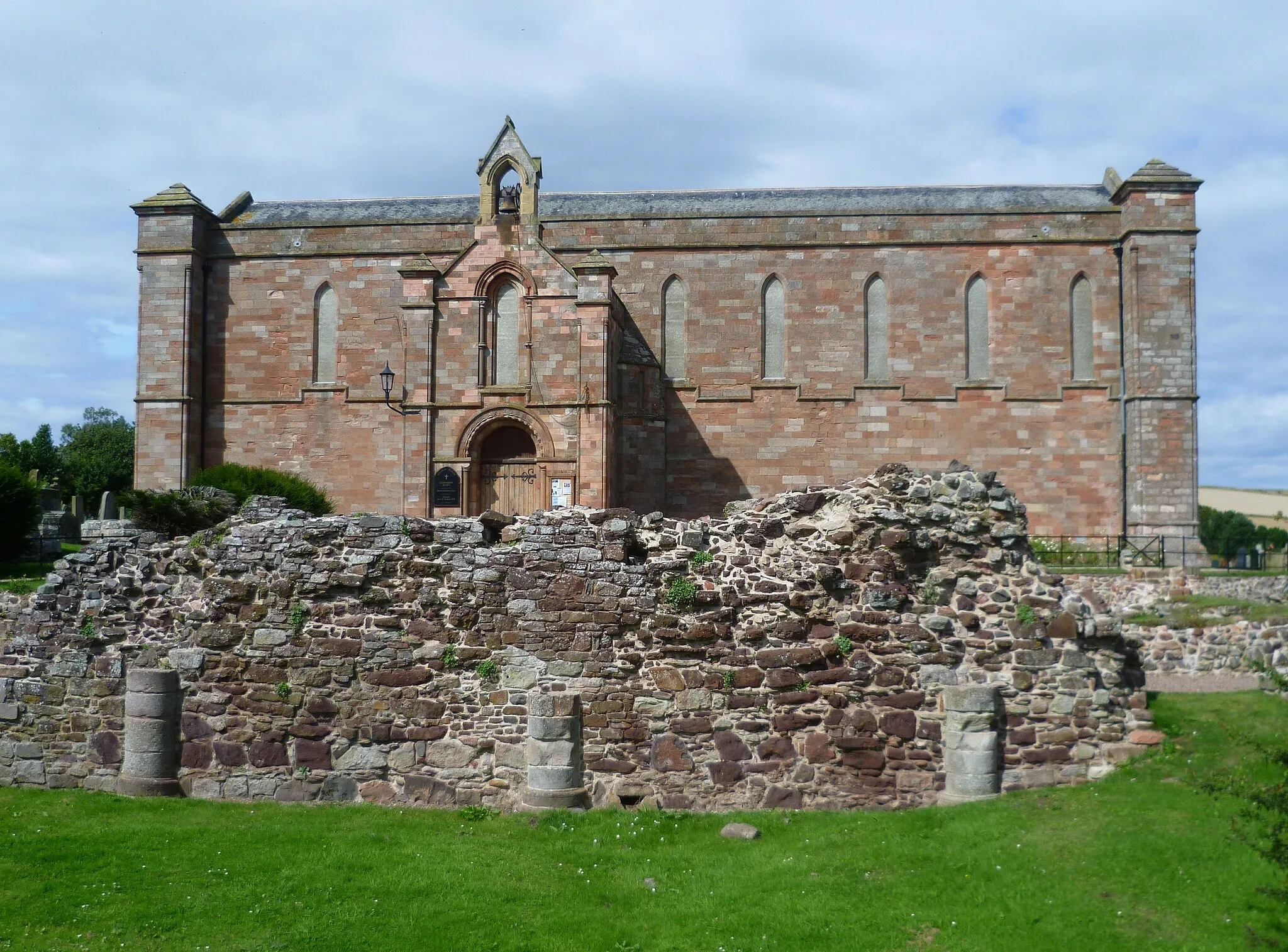 Photo showing: Coldingham Parish Church, built using stones taken from the ruined medieval priory. Remains of the monastic buildings can be seen in the foreground.