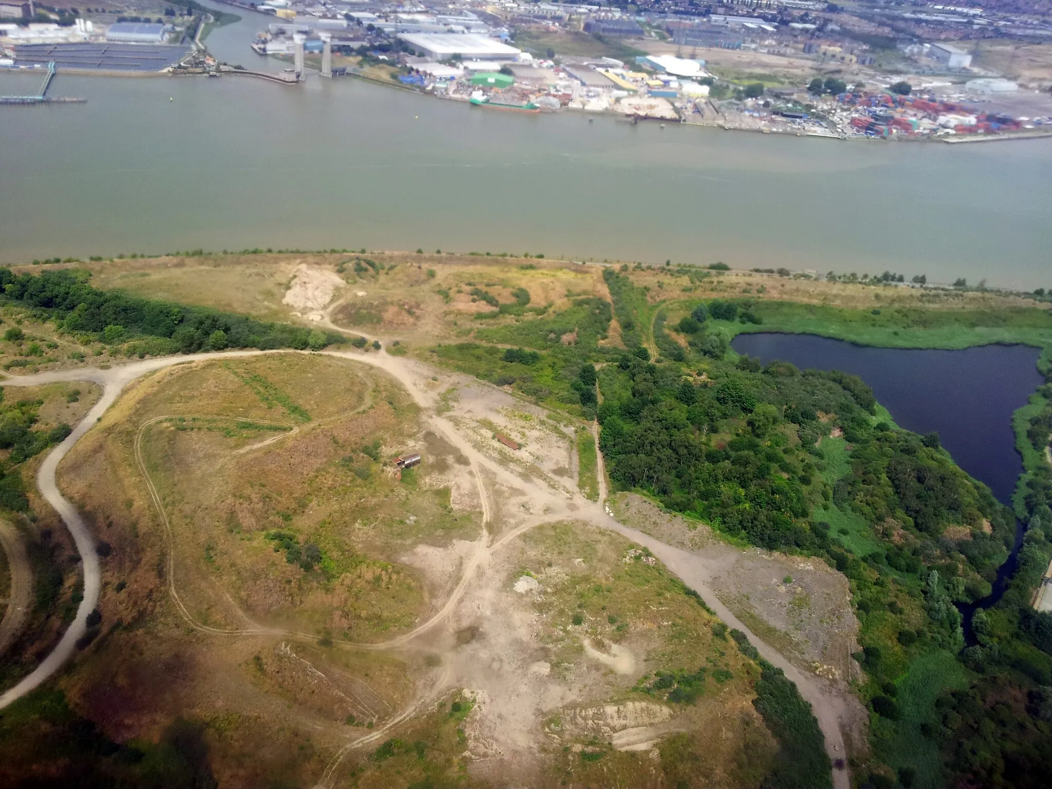 Photo showing: Aerial view of wasteland along the Thames in Thamesmead Moorings, South East London. The land was formerly part of the Royal Arsenal in Woolwich. The lake to the right is Silvermere.