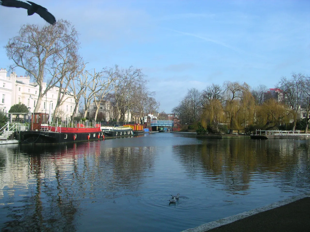 Photo showing: Little Venice basin viewed from the western end looking north-east towards the Regents Canal corner, with the island on the right and white Regency style terraces overlooking the basin.