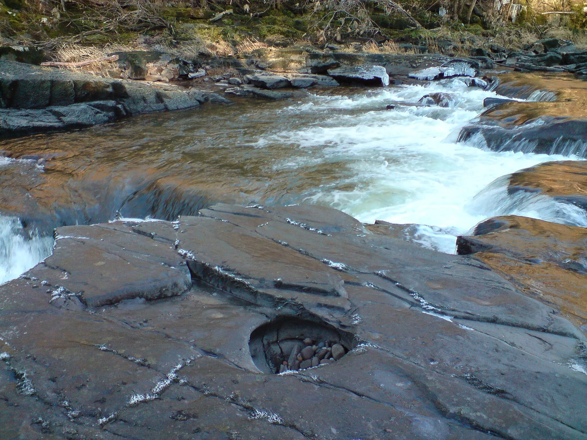 Photo showing: River Clyde A pothole on a rockshelf on the bed of the River Clyde above Stonebyres Falls.  These features are responsible for corrading and thus lowering river beds through vertical erosion.