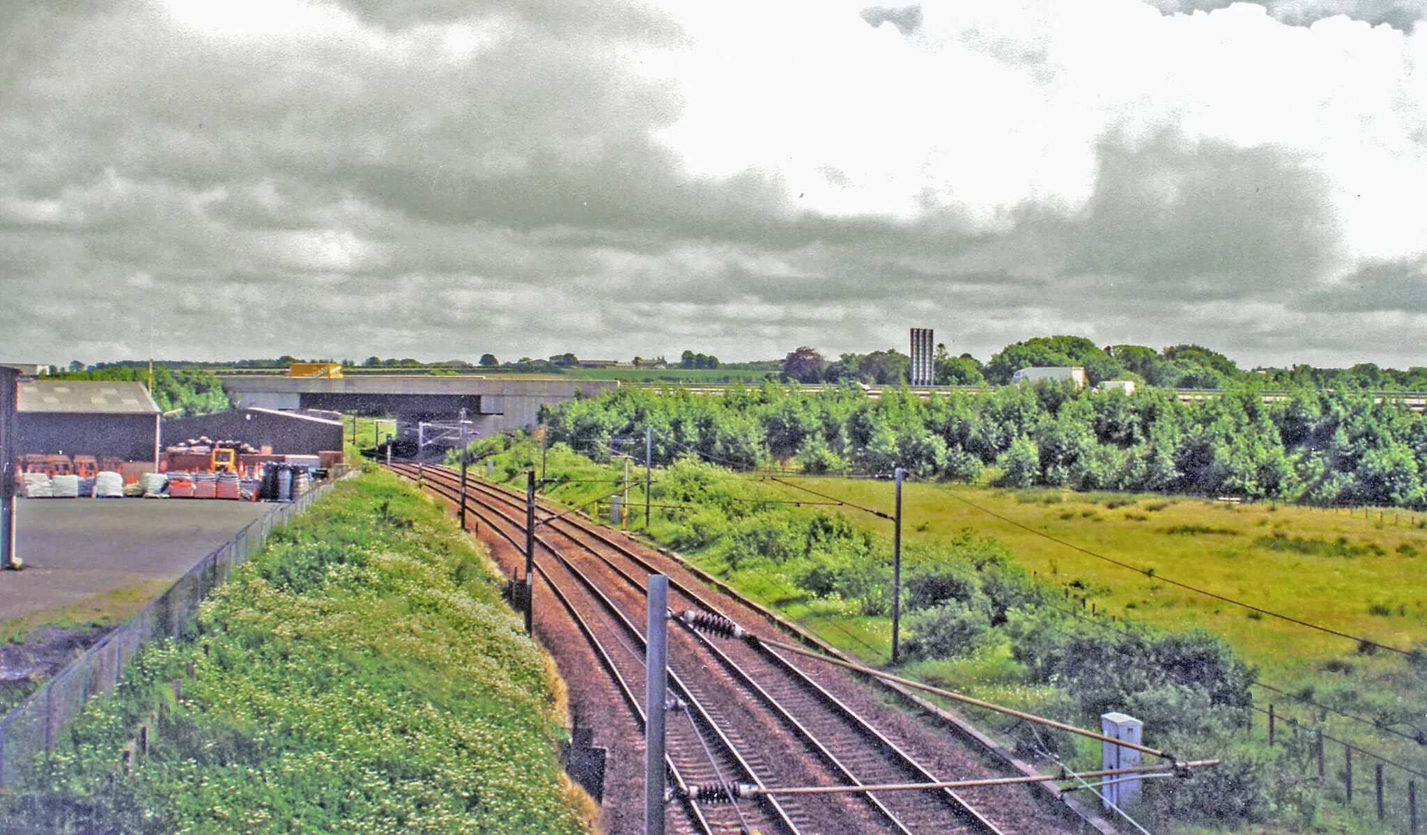 Photo showing: Site of former Kirtlebridge station, WCML 2000.
View southward from B722 to the large bridge of the new A74(M). This is situated where the station had been, until it closed 13/6/60 to passengers (6/4/64 to goods). The view is up the ex-Caledonian Railway (Glasgow - Carlisle) section of the West Coast Main Line, electrified 1974. Off to the right used to be the branch line to Annan (Shawhill) and over the Solway Viaduct to Brayton on the Maryport & Carlisle Railway; this lasted to Brayton only until 20/5/21, to Annan for passengers until 27/4/31 (goods 28/2/55, however).
