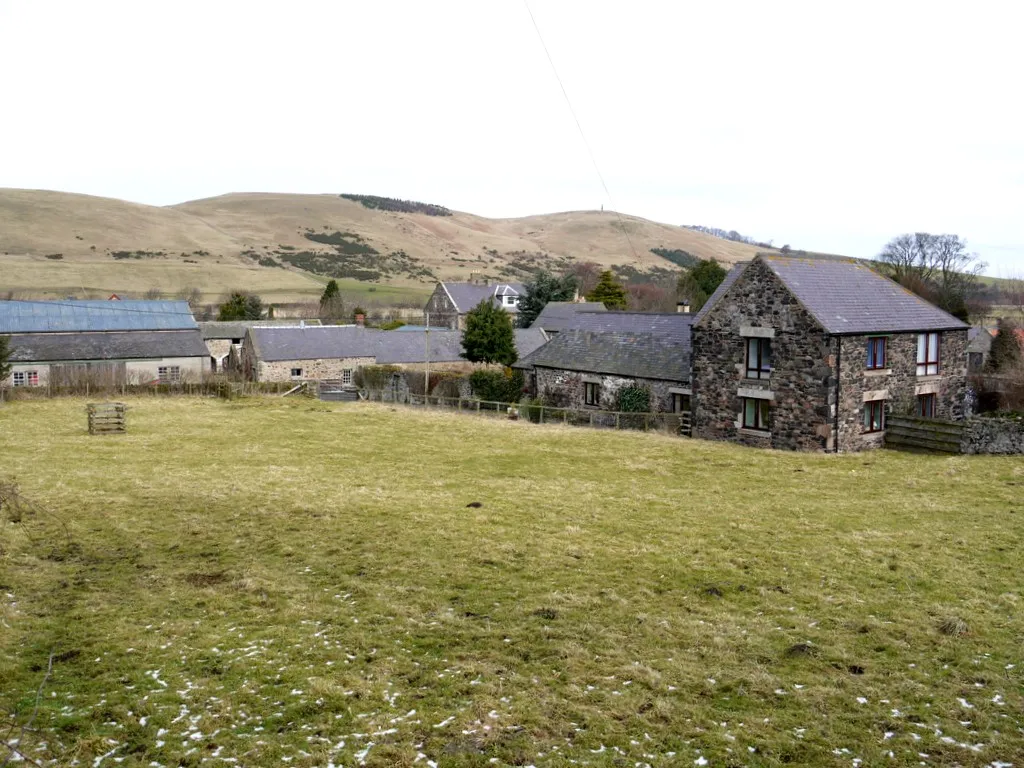 Photo showing: Kirknewton The shrunken medieval village of Kirknewton, also known as East Newton, lies below the much smaller settlement seen today. It was first recorded in the late 13th century http://www.keystothepast.info/durhamcc/K2P.nsf/K2PDetail?readform&PRN=N2053
The building on the right is the old Kirknewton water mill, now converted for domestic use http://www.northumberlandnationalpark.org.uk/kirknewtonwatermills