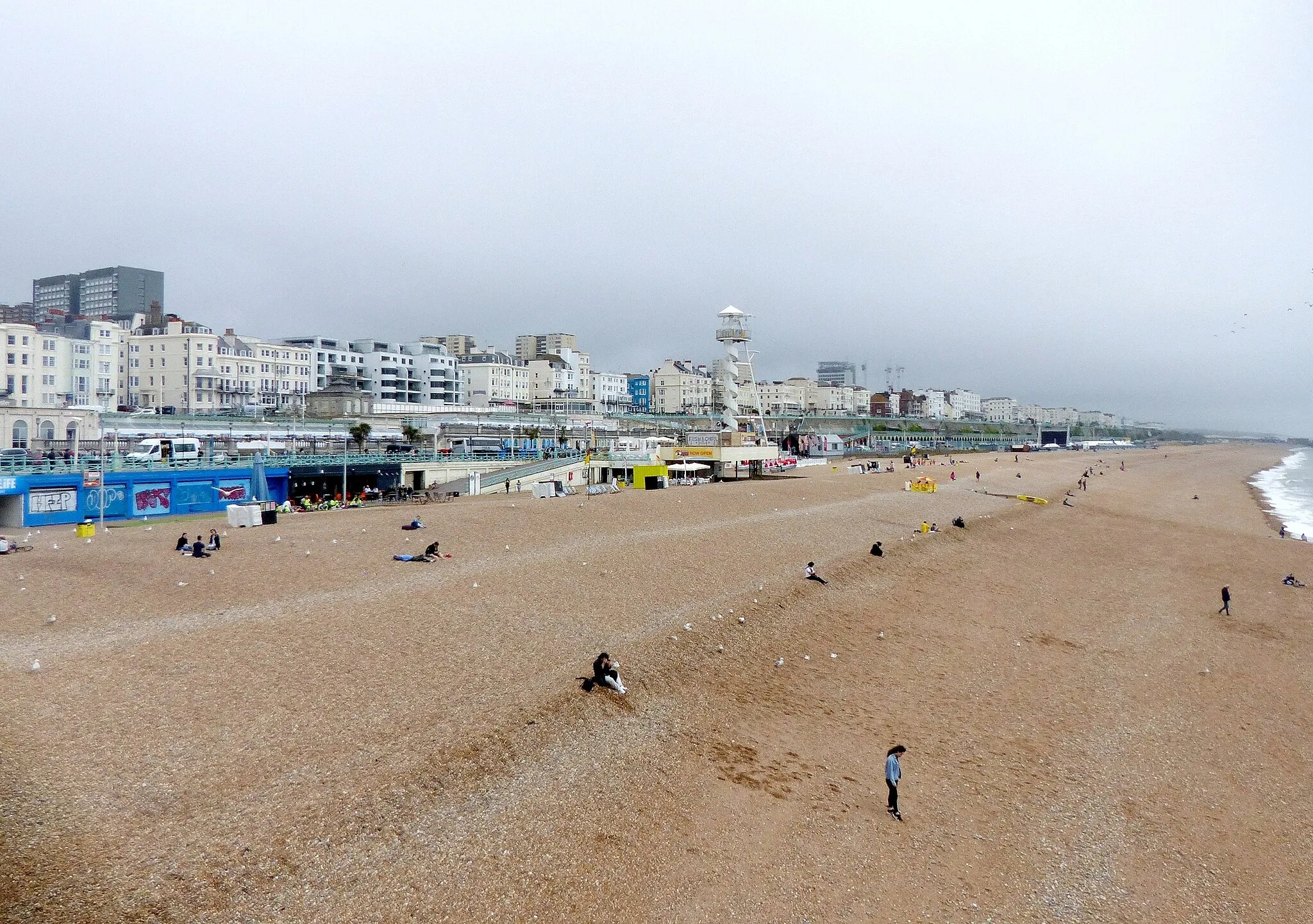 Photo showing: Brighton Beach, looking from the Palace Pier eastwards. The white spiral tower is a Zip line ride that lands at the black rectangle on the right.