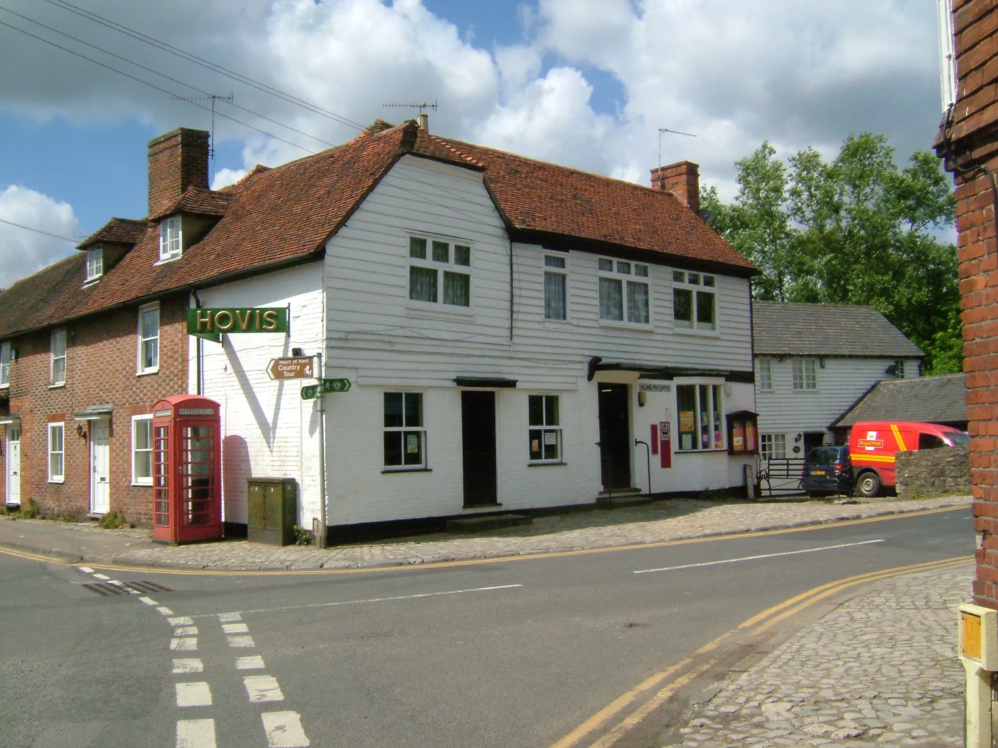 Photo showing: Yalding, the junction of High Street and Lees Road showing the post office, with telephone box. The building is white shiplap, with Kentish peg tile roof, behind building with decorative brickwork, and dormer window in the pegtile roof. This spot lies on the Greensand Way, and the Heart of Kent Country Tour. Camera location 51° 13′ 24.6″ N, 0° 25′ 44.4″ E View this and other nearby images on: OpenStreetMap 51.223500;    0.429000