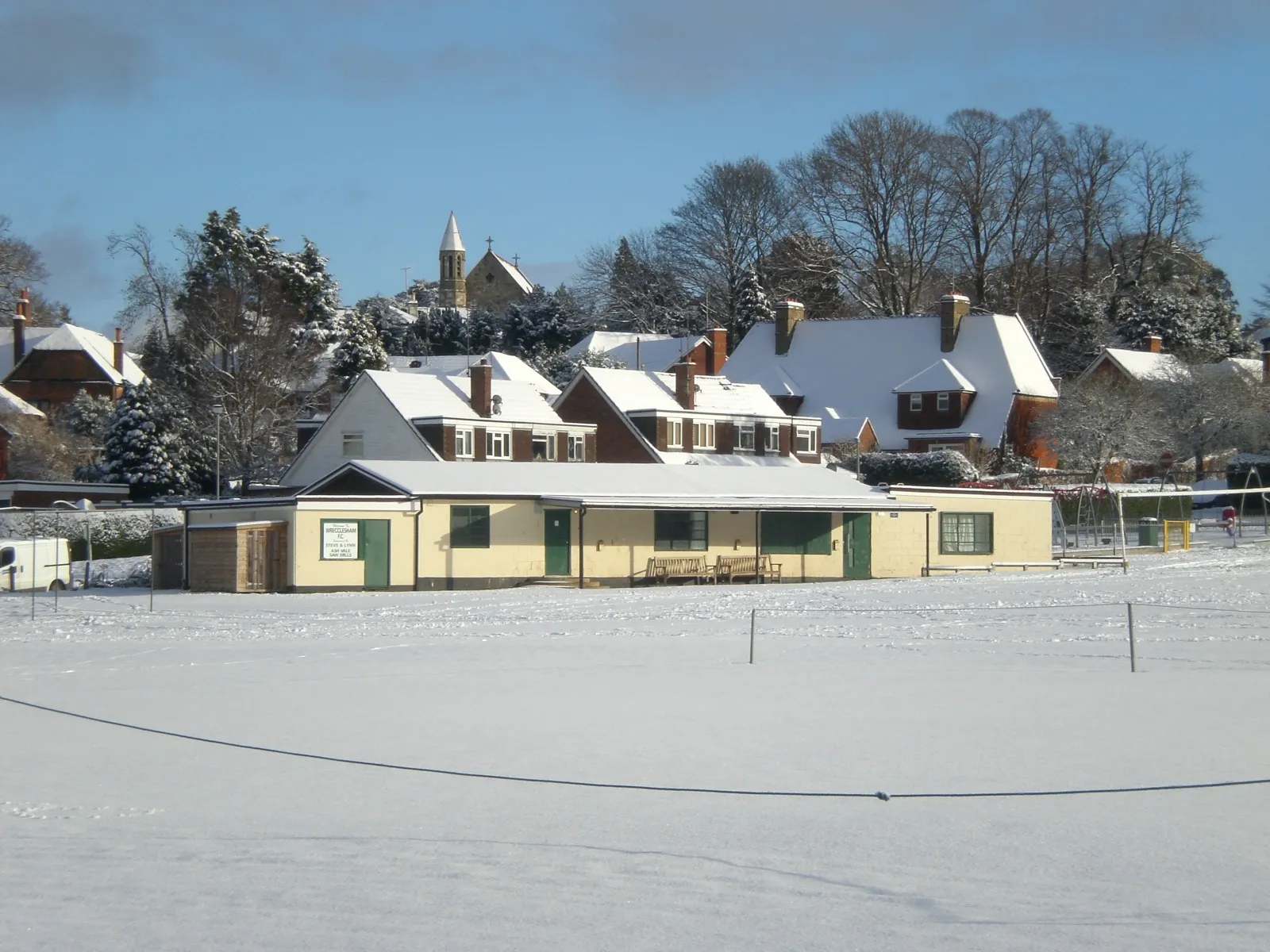 Photo showing: Photo of Wrecclesham Recreation Ground Pavilion in snow with St. Peter's Church in the background