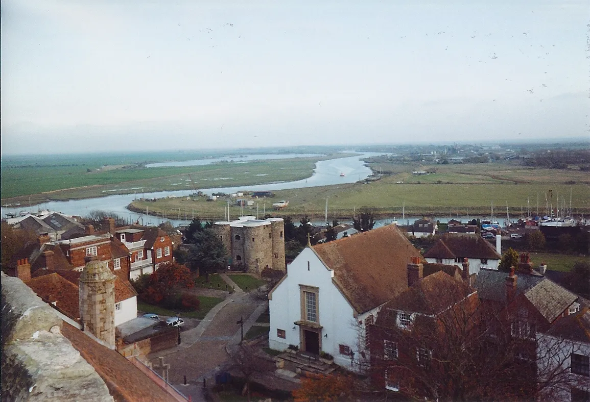 Photo showing: View from the tower of St Mary's church, Rye, East Sussex, southern England. The white-painted building is the Methodist church. The Ypres Tower in the centre-left marks the cliff-edge which defines the citadel. Below the cliff, roofs of buildings beside the River Tillingham can be seen, with yacht masts beyond. The river joins the River Rother and winds across Romney Marshes to the English Channel.