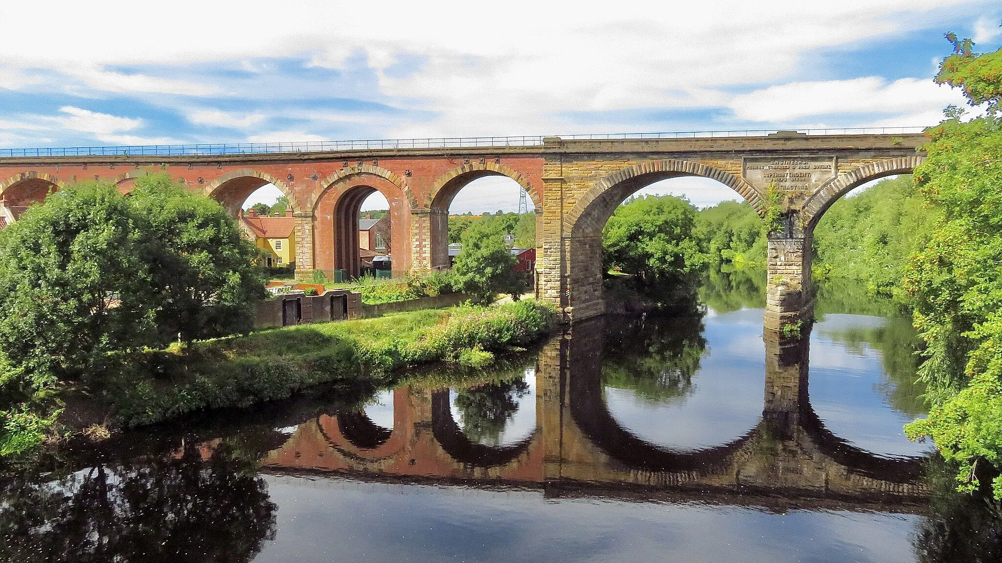 Photo showing: The viaduct extends for over 2,280 feet in a north/south direction over the town of Yarm and across the River Tees. It consists of 43 arches; 41 of them are 40 feet span and are constructed of 7.5 million red bricks. The other two arches are constructed from stone and are 67 feet across with one pier standing in the river. The two spans across the river are composed of 139,000 cubic feet of stone and are skewed across the river by 20 degrees. On the downstream side of the viaduct (eastern side) is a large plaque set into the stone section of where the bridge spans the river. This commemorates the engineers and contractors on the project.