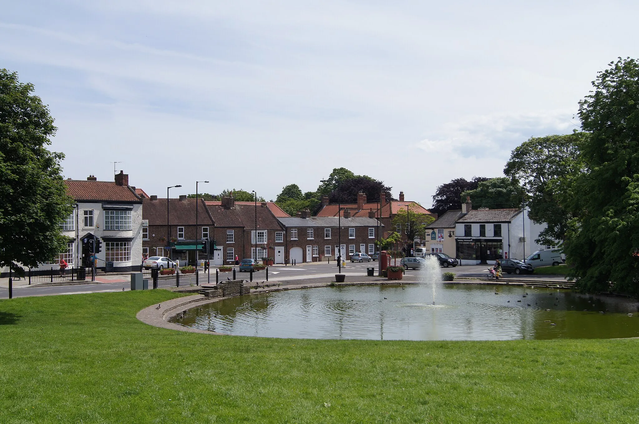 Photo showing: Norton Village Green with duckpond and fountain.
Picture taken in June 2012, facing south east towards the north end of the High Street. The Unicorn Pub can be seen behind the fountain. Building opposite the pedestrian crossing is the former blacksmiths forge, now a newsagent shop and cafe.