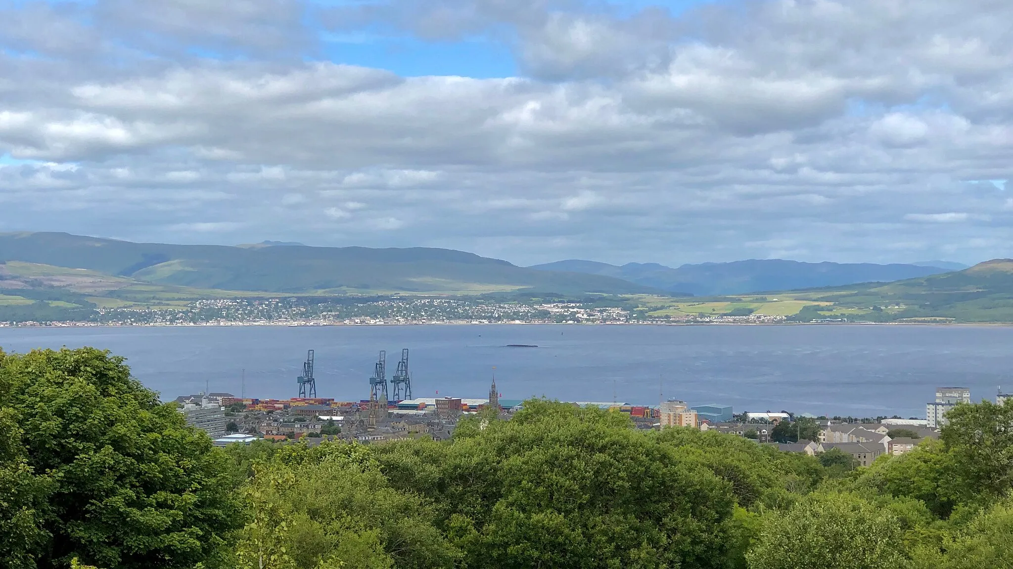 Photo showing: View from The Cut at Overton, Greenock, down over the Tail of the Bank to Helensburgh. The wreck of the sugar ship Captayannis marks the extent of the deep water anchorage. To the right of the Ocean Terminal container cranes, the red brick Glebe Sugar Refinery and the spire of St. George's North Church Of Scotland, George Square, are listed buildings.