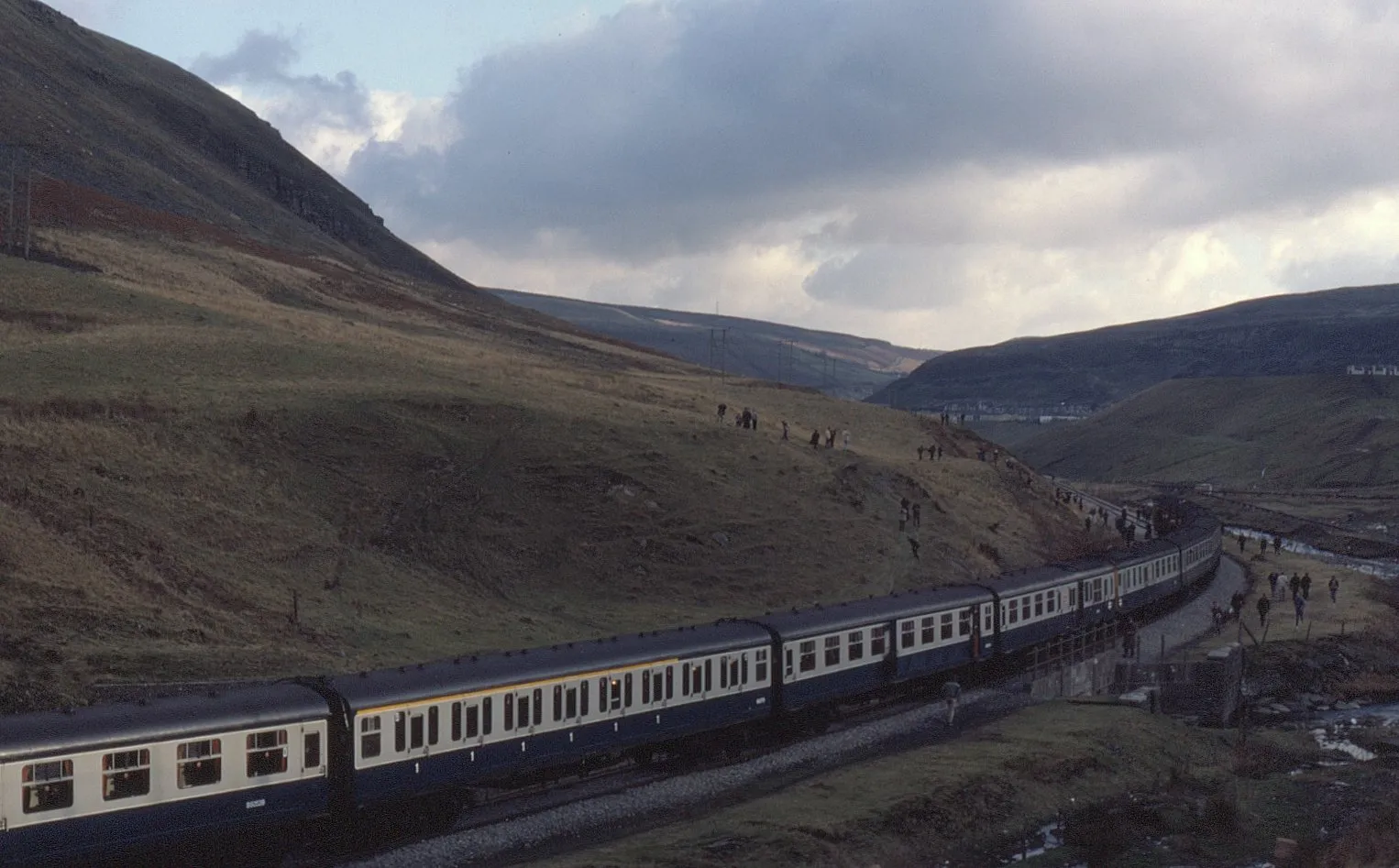 Photo showing: 12-car "Hastings" DEMU formation a long way from home. As already detailed with other photographs, the mid-1980s were to be the swansong for the popular units. As such, they were chartered for some long distance railtours well beyond the Southern Region.

On 5 January 1985, 6L sets 1017 and 1032 were assigned to work 1Z27, 07:20 Watford Junction through to several branches in South Wales. Seen here at Maerdy Colliery is the "Cyrmru DEMU" tour during a 12 minute photo-stop.  It was amazing how often several hundred participants managed to leap off the train, climb up steep embankments and then rejoin the train in the short space of time! Tour operator was again Hertfordshire Railtours. Myself and many others living in the South East of England would be regular travelers as they would start and pick up in the London/M25 catchment area.