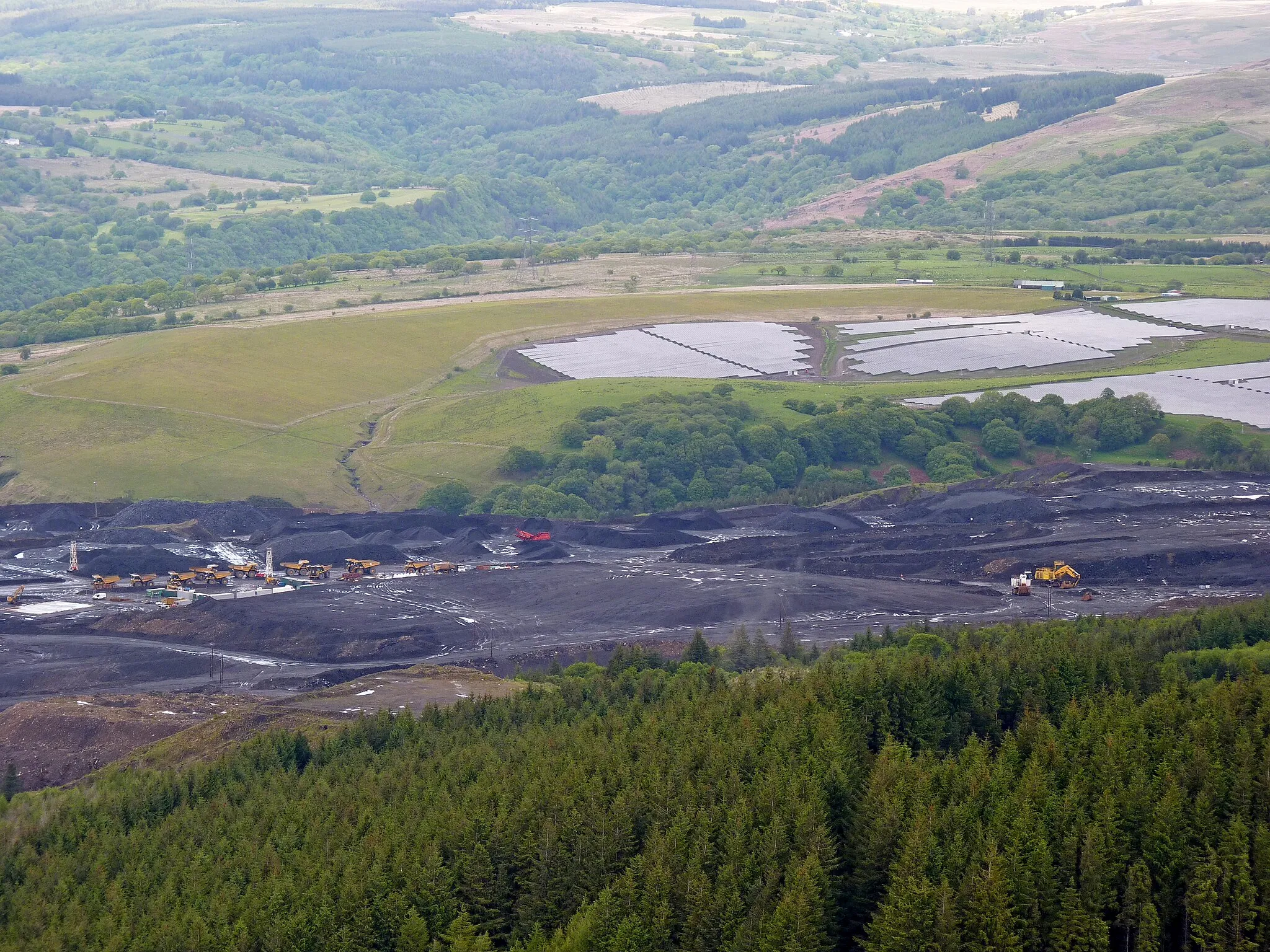 Photo showing: Open cast coal mine above Cwmgwrach, in the Neath Valley, South Wales. For most of the 19th and 20th centuries these coal seems were mined through underground tunnels. Now the only coal being extracted is through open cast mining. Beyond the open cast are photoelectric panels, and then the slopes of the upper neath valley, leading into the Brecon Beacons.