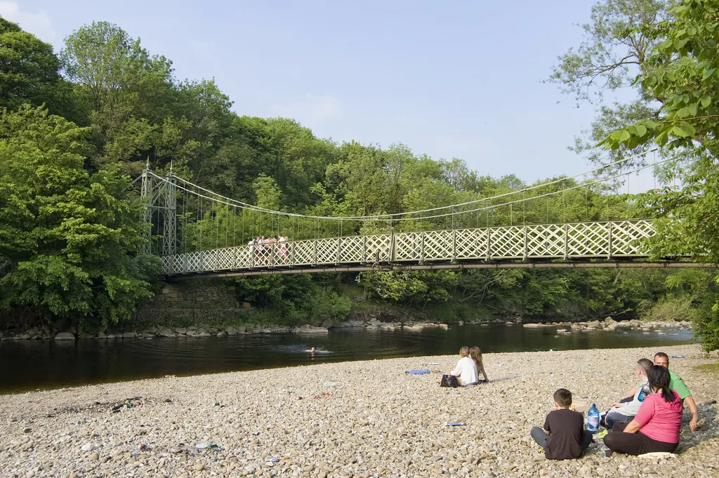 Photo showing: Teens relax in late afternoon sunshine on a smooth pebbled beach; watching their testosterone-fuelled peers leap from an old suspension bridge over the Wharfe. A copy of this file can be found online in its original resolution at this address.