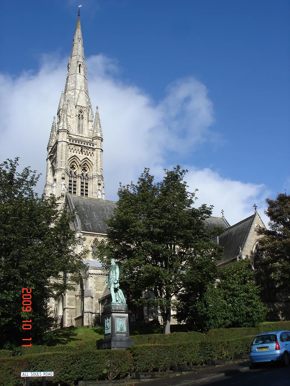 Photo showing: All Saints church, Halifax, designed by Sir Gilbert Scott for Edward Ackroyd, whose statue stands in the foreground.